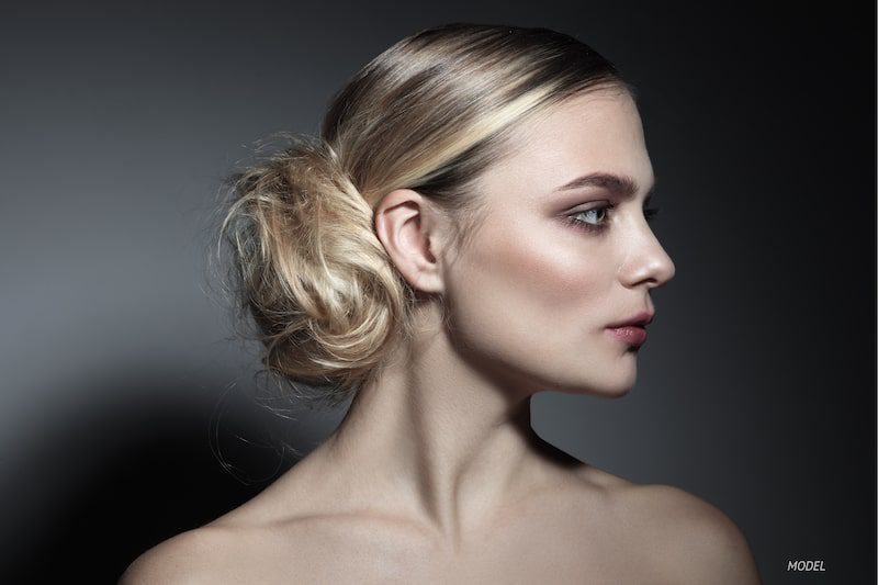 Profile of young woman with high cheekbones against gray background.