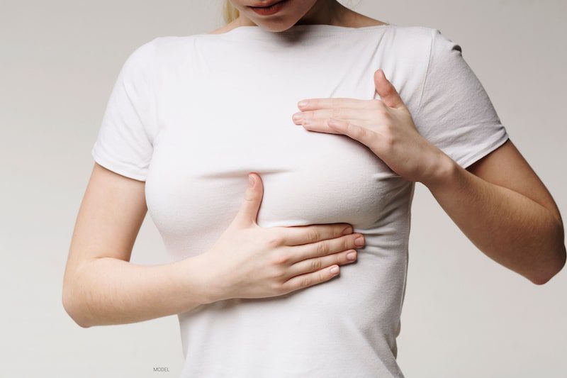 Woman squeezing her breast over her t-shirt.